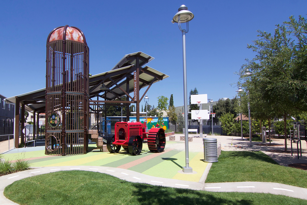 madison ave playground with red tractor and brown metal silo to climb in and on.